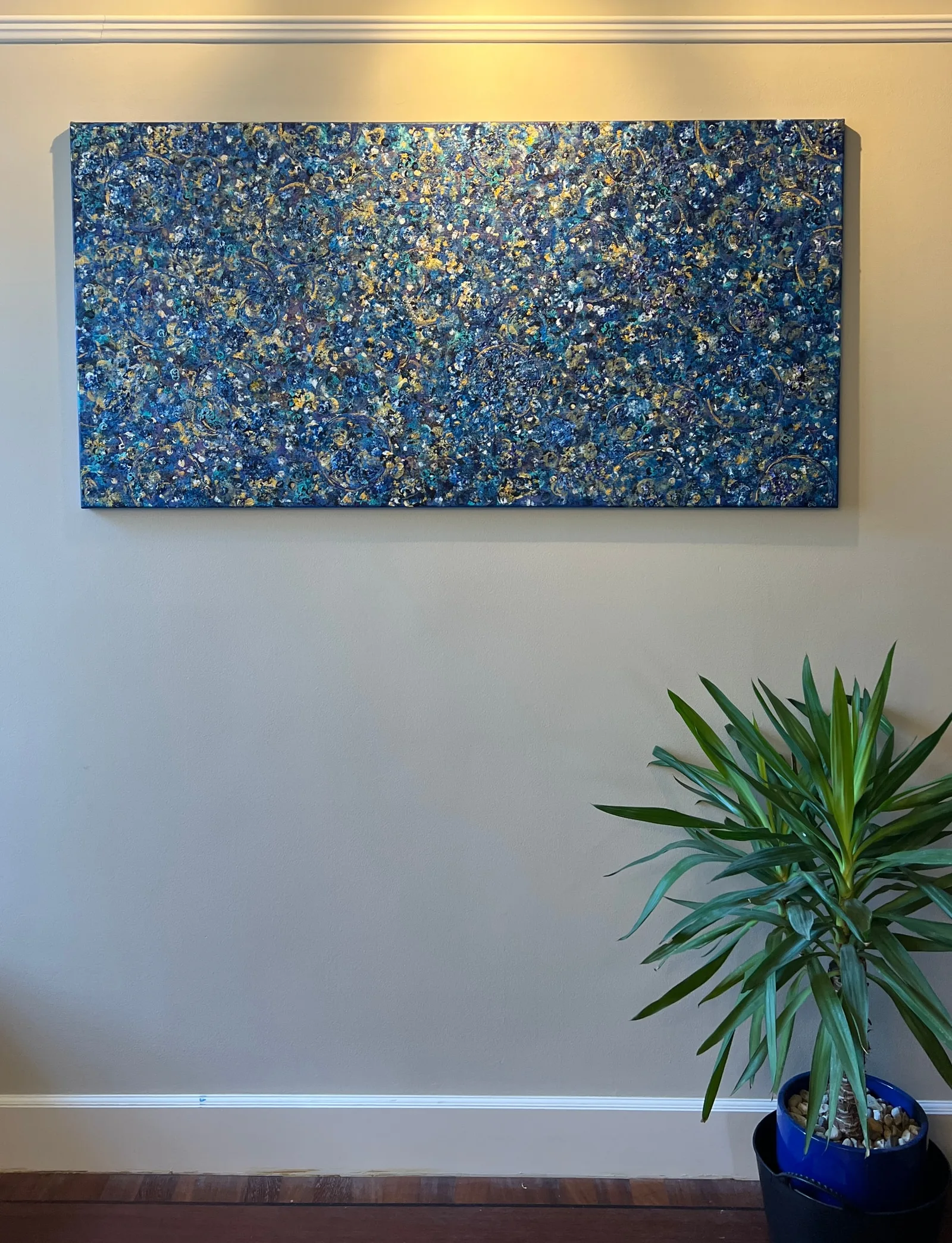 Beginning displayed unframed on a wall above a green plant, showing the painting at room scale.