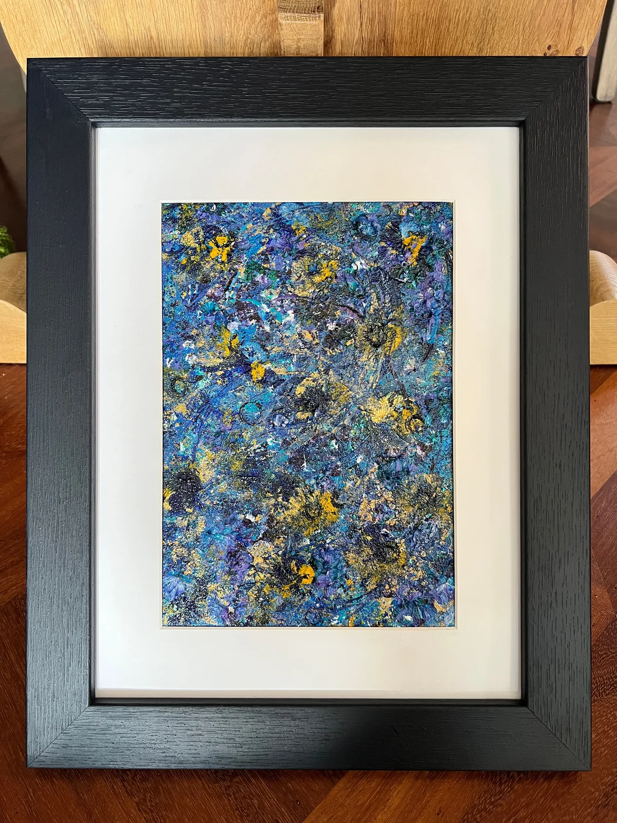 Beginning - Sunflower Edition, a textured blue, violet and yellow abstract painting with a white mount and black frame against a white wall.