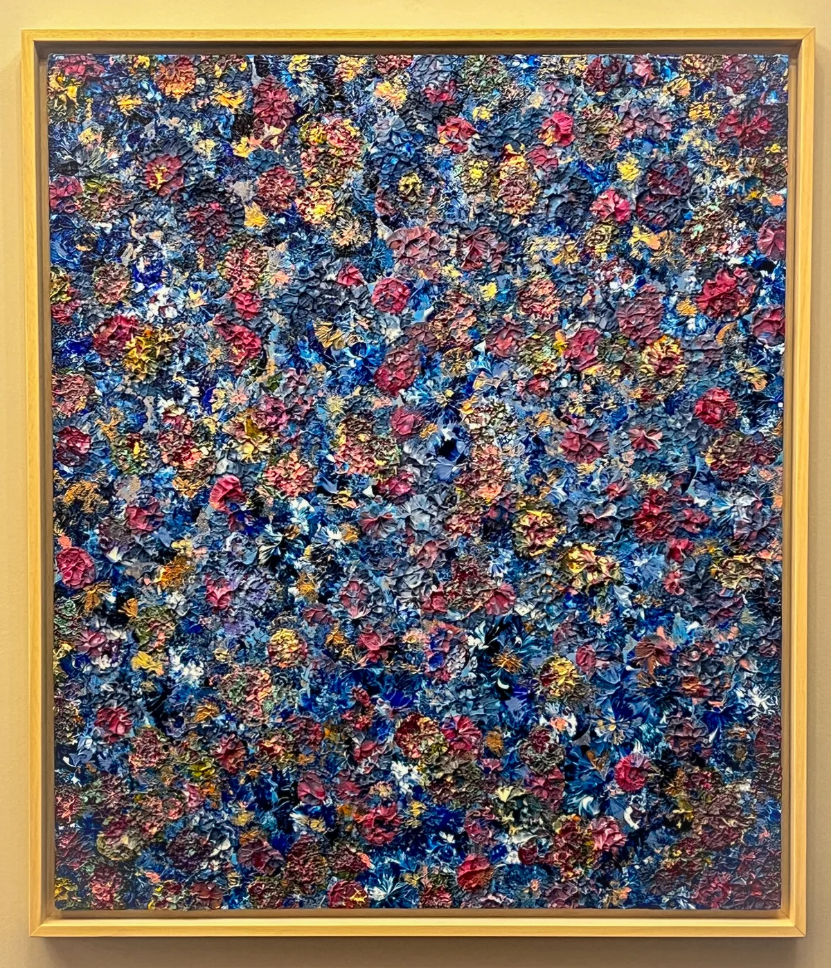 Bloom Where You Are Planted, a textured blue, pink and gold abstract painting in a natural wooden shadowbox frame against a white background.