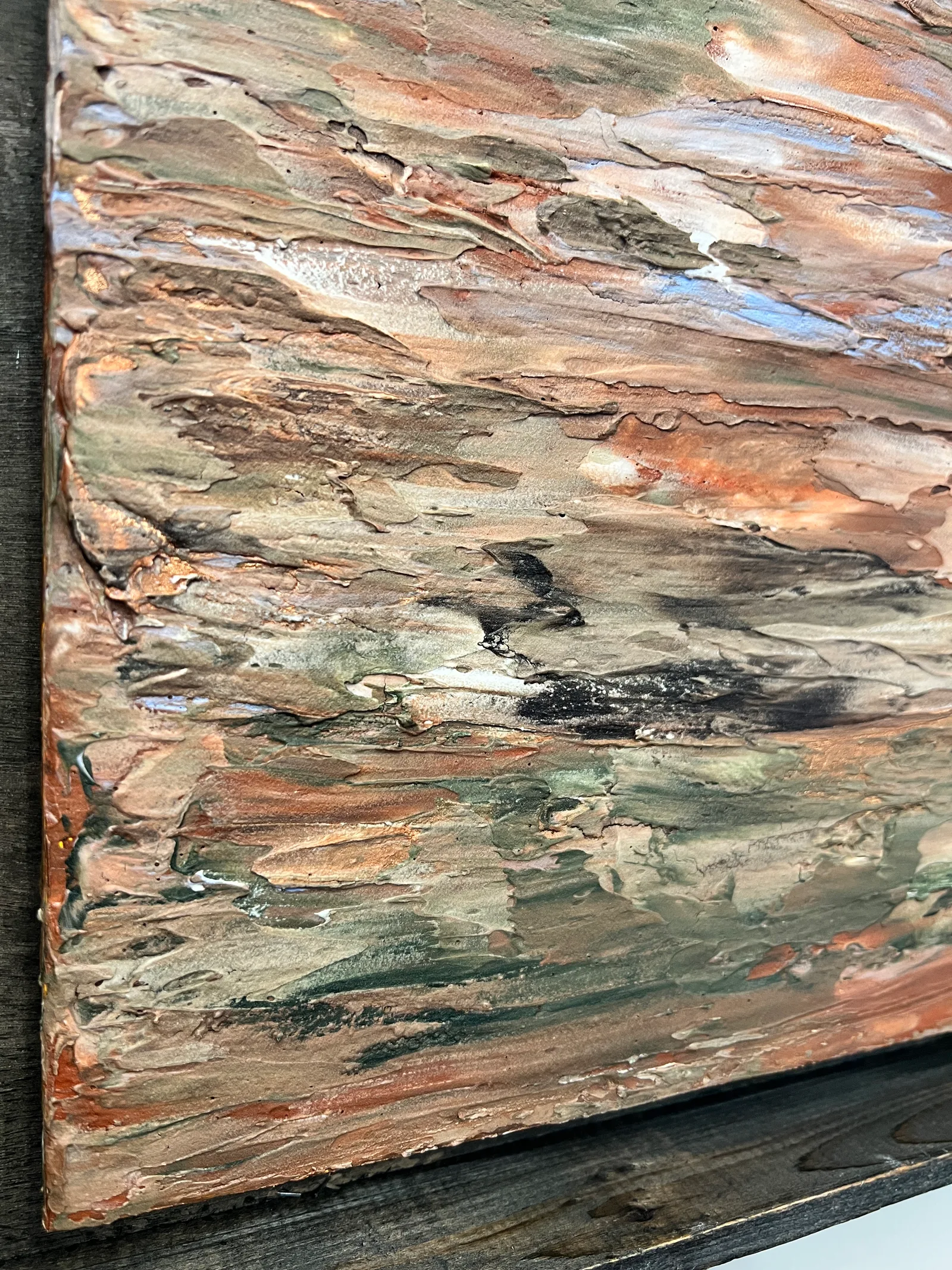 Angled close-up of the layered terracotta, green and pale blue paint in Georgia Clay beside its dark frame.