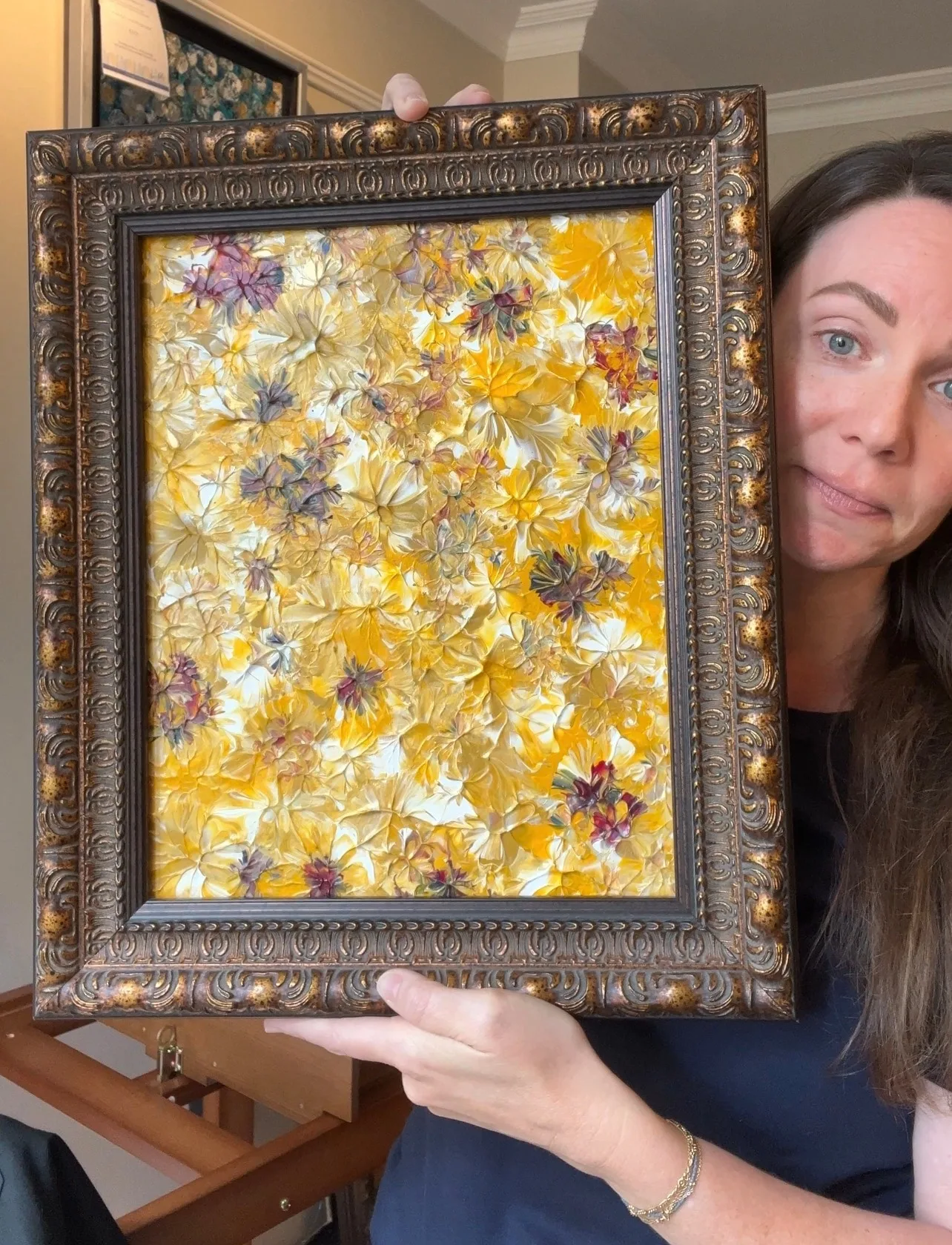 Kelly holding Golden Meadows, showing the scale of its ornate frame and textured floral painting.