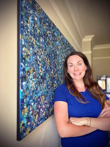 Kelly standing beside a large blue abstract artwork.