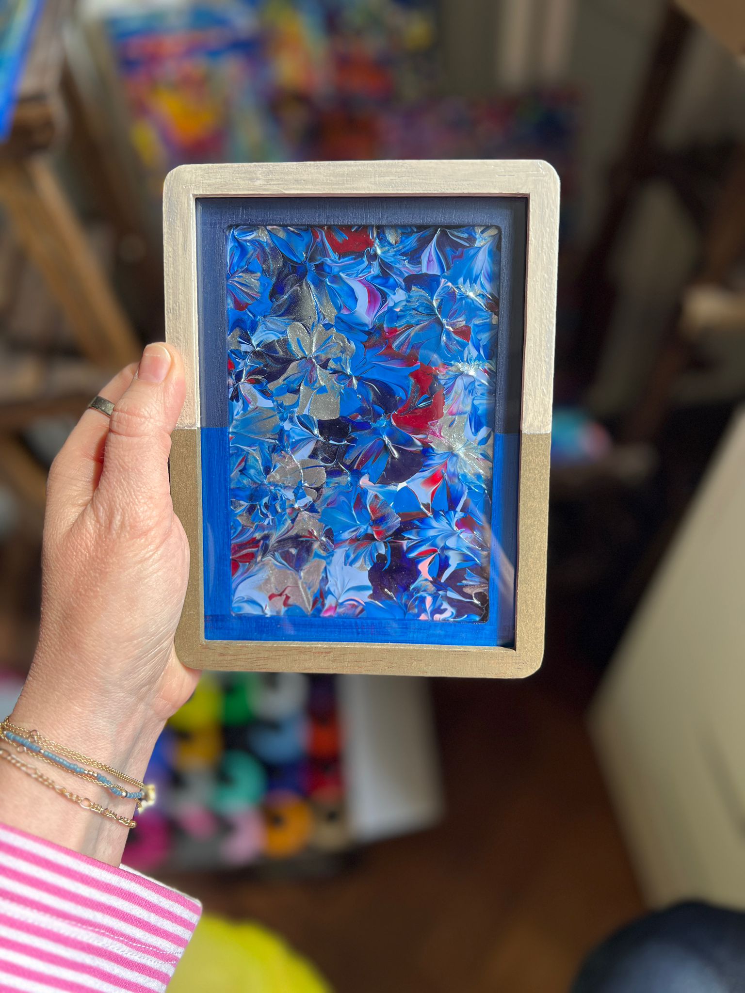 A small framed KNH abstract artwork with blue, silver, red, and gold details in a gold frame.