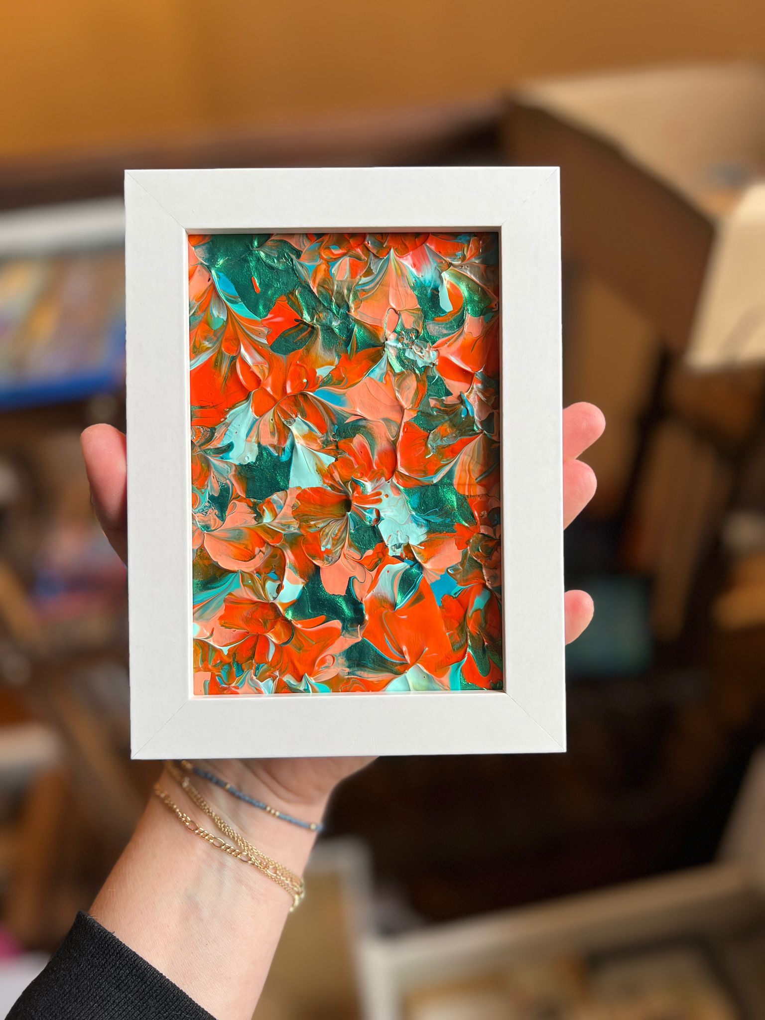 A small framed KNH abstract artwork with orange, coral, teal, and green movement in a white frame.