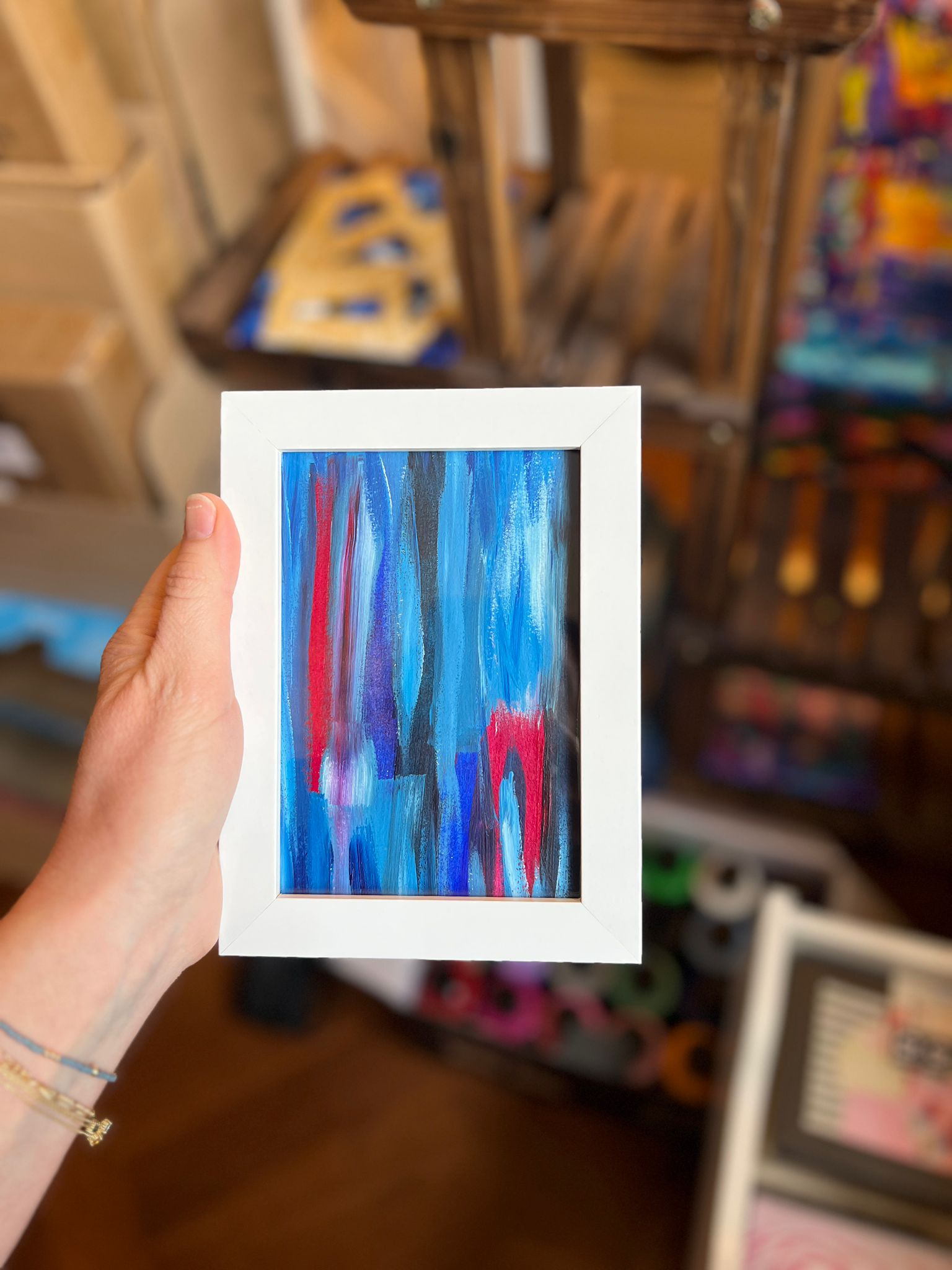 A small framed KNH abstract artwork with blue vertical marks and magenta accents in a white frame.