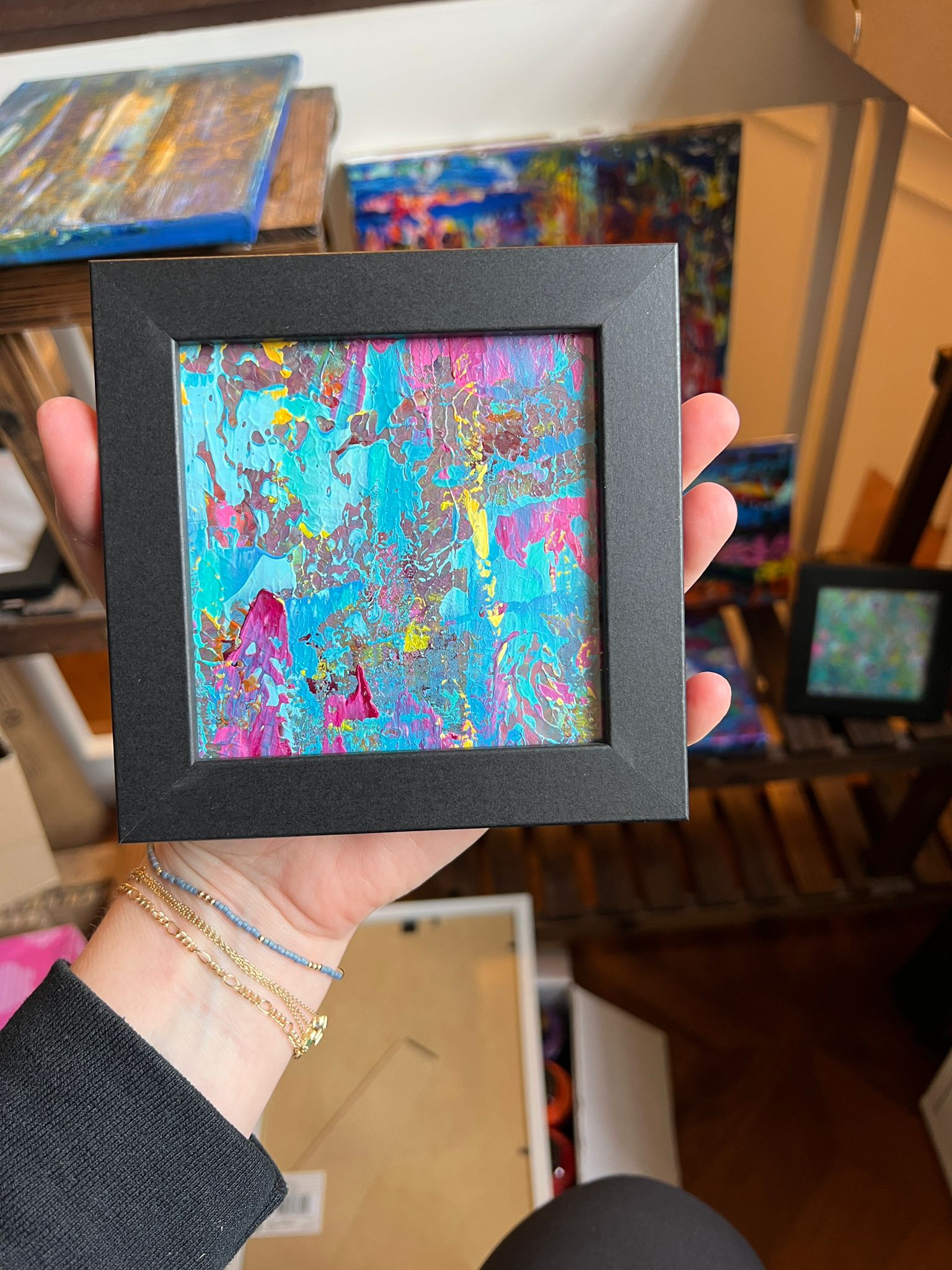 A small framed KNH abstract artwork with bright turquoise, magenta, and yellow texture in a black frame.