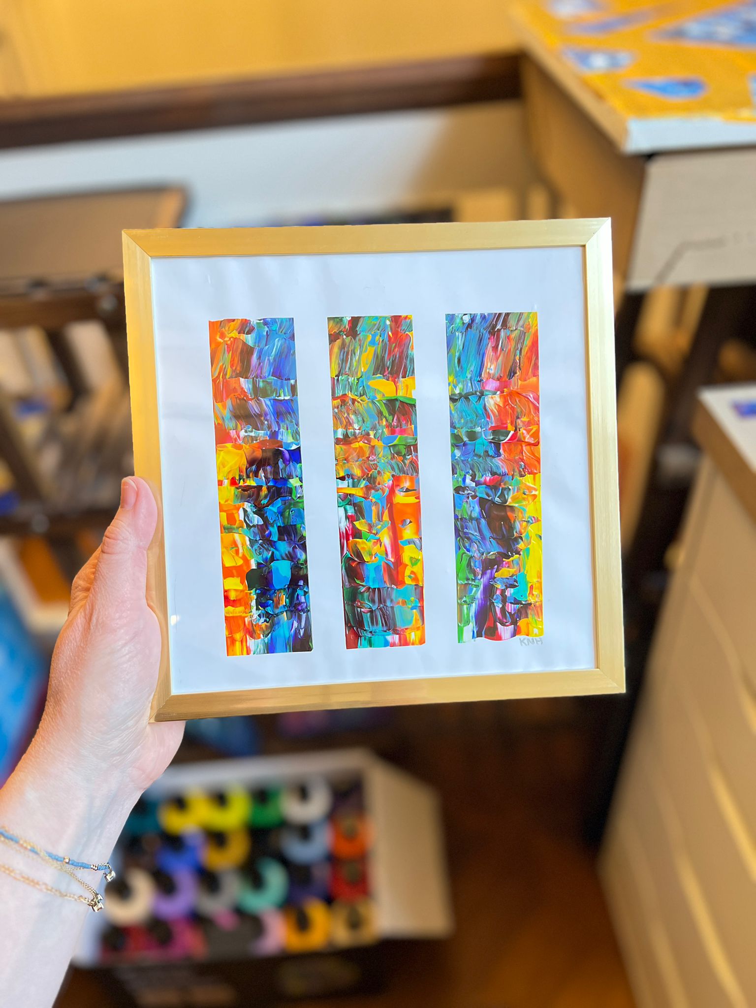 A framed KNH abstract painting with three bright vertical color studies.